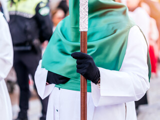 Close up of a nazarene in green hood holding a silver ceremonial procession cross.