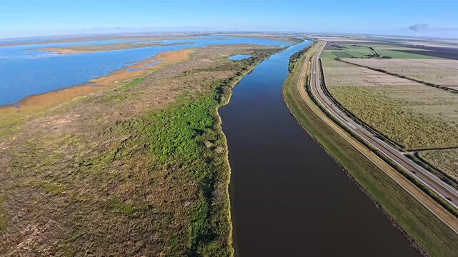 Aerial view of the waterway, a ribbon of dark water contrasting with the lush green vegetation and adjacent highway, Lake Okeechobee, Florida, United States.