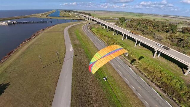 Aerial view of a bridge over water with a paraglider, showcasing the contrast between the dark water and the lush green landscape, Lake Okeechobee, Florida, United States.