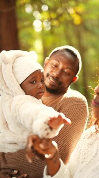 A woman is holding a baby and a man is holding a brownie. The woman is smiling and the baby is looking at the brownie. Scene is happy and playful