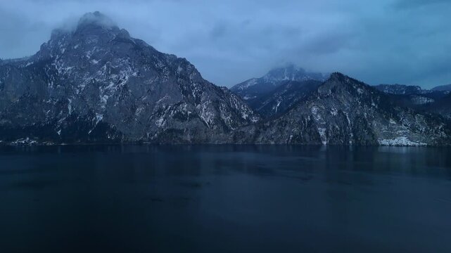 Aerial drone flying backward over alpine mountain range and Traunsee lake, Austria