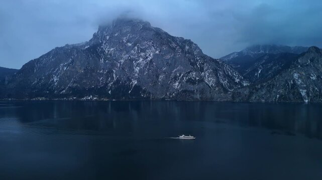 Aerial drone side view of boat moving forward on alpine lake with snowy mountain winter landscape