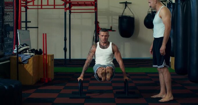 Male mixed martial artist doing arm exercises using parallel bars.