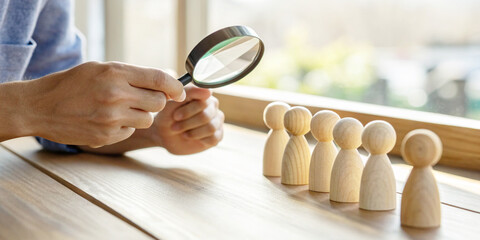 Business background.Hand is holding a magnifying glass to examine a wooden statue along with the concept of selecting people for job applications.