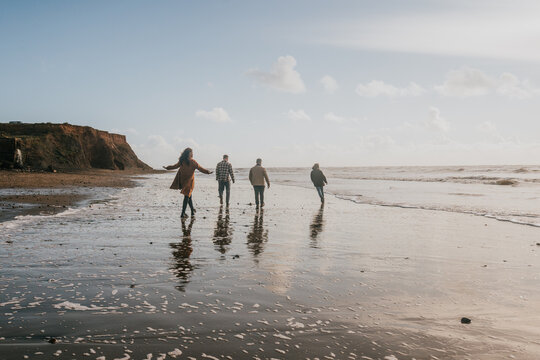 A family of four is walking on the beach, enjoying the ocean view. Scene is lighthearted and joyful, as the family members are all smiling and having a good time