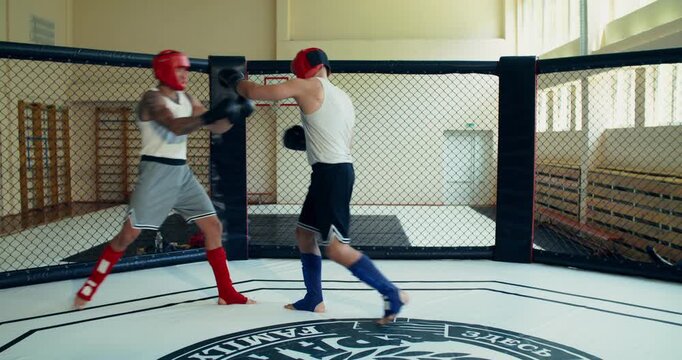 Two fighters wearing helmets spar in the ring.. Two MMA fighters spar in the ring.
