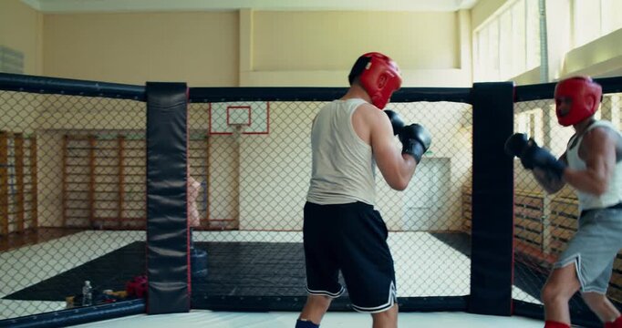Two fighters wearing red helmets and gloves practice techniques during a training fight. Two MMA fighters spar in the ring.