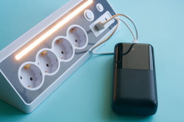 White extension cord with built-in night lamp and fast charging ports connected to an external battery. Top view of electrical equipment and USB cable. Photo