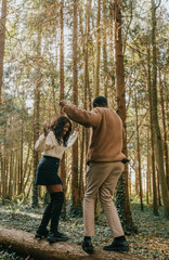 Fototapeta premium A man and woman are dancing on a log in a forest. The man is wearing a brown jacket and the woman is wearing a white shirt and black skirt. Scene is lighthearted and playful