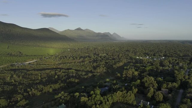 Drone facing east lowers over a forested community at base of the Tsitsikamma Mountains at sunset in Stormsrivier, Eastern Cape, South Africa