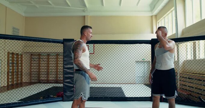Two male MMA fighters discuss grappling techniques in the ring. Two MMA fighters spar in the ring.