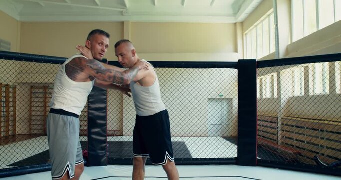 Mixed martial artists practice grappling techniques in the ring. Two MMA fighters spar in the ring.