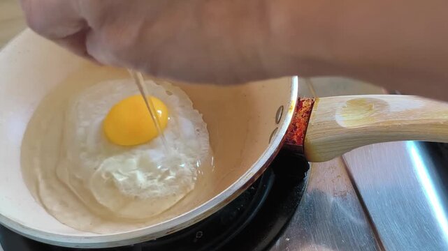 Cracking and Frying an Egg in a Beige Pan on a Gas Stove.