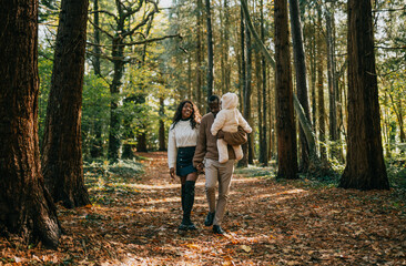 Fototapeta premium A couple and their child are walking through a forest. The man is holding a teddy bear