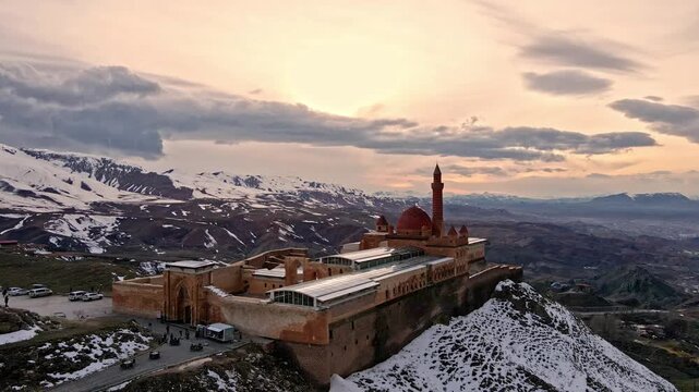 A cinematic aerial view of Ishak Pasha Palace in Ağrı, Turkey, surrounded by snowy mountains at sunset. Ideal for history, architecture, travel, culture, and landscape footage.