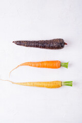 Purple, orange, and yellow carrots on a white background. Cooking with farmers products. Top view