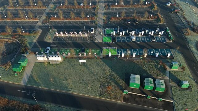 Rugby, United Kingdom - 31 December 2025: Aerial view of rows of electric vehicles charging at a green station amidst a large car park.