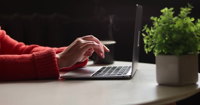 Hand of woman using laptop computer to work, typing at home and scrolling, while sitting on table workplace at night, Close-up of young women hand