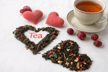A white cup of tea, tea poured into hearts on the table, pink hearts, candies