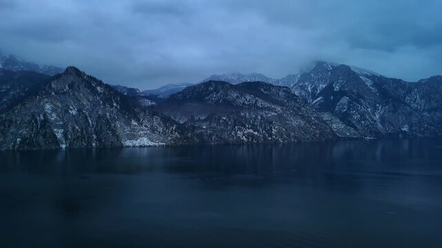 Aerial drone view of mountain range enclosing alpine lake Traunsee in Austria with foggy peaks and snowy winter landscape
