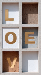 LOVE letters arranged in gold on concrete formwork panels, each letter placed in separate square compartment, creating modern and minimalistic wall art with warm, romantic feeling
