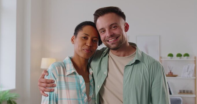 Portrait of young happy multiethnic couple standing at home together and hugging. Smiling family man and woman looking cheerful at camera indoor. Love and harmonic relationships concept. 4k video.