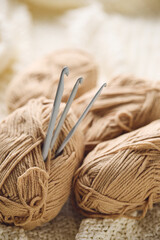 Crochet hooks and balls of beige and brown yarn on white knitted background. Knitting, crocheting supplies.