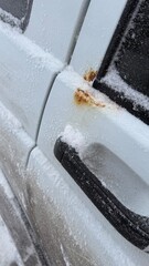 Close up view of rust on car door covered with snow and ice caused by winter road salt showing corrosion damage and vehicle maintenance problem
