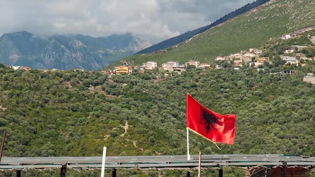 Albanische Flagge weht &uuml;ber Berglandschaft mit verstreutem Dorf, Bunec, Qark Vlora, Albanien
