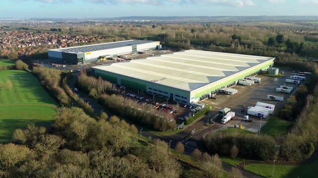 Milton Keynes, United Kingdom - 20 December 2025: Aerial view of large DHL warehouses with trucks and cars in the parking lot surrounded by green fields.