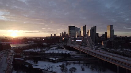 Boston, United States - 24 December 2025: Aerial view of the Zakim Bridge under a dramatic, cloudy sky, contrasting with snow-covered ground and the skyline.