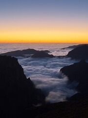 madeira pico del ray A spectacular sunset bathes the horizon in golden light, while dark mountain peaks rise from a dense, soft sea of clouds.
