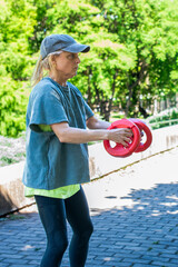 Middle aged woman training with weight plates during an outdoor workout in a park