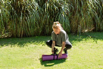 Middle aged woman rolling up her purple yoga mat after an outdoor workout in a park