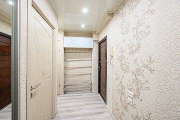 Narrow hallway with floral wallpaper, light wooden doors, mirrored wardrobe, light grey laminate...