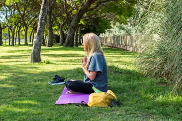 Mindful female sitting on a purple mat for a zen yoga session in the park