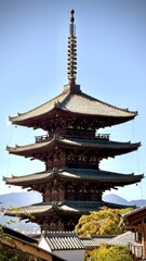 A historic five-story wooden pagoda towers majestically against distant mountains into the blue sky above the traditional roofs of the old town.