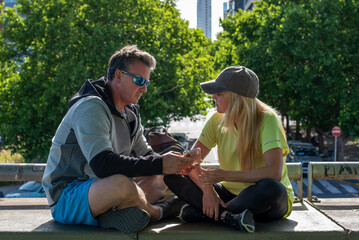 Middle aged couple sitting together and looking at a smartphone after an outdoor workout