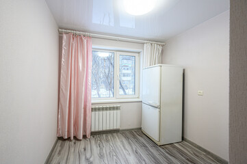 Fototapeta premium Small room with light grey laminate floor, white walls, double window with pink and white curtains, white radiator, white fridge, simple ceiling light