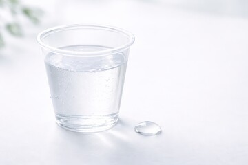 A Transparent Cup of Water with a Small Droplet on a Smooth Surface, Highlighting Clarity and Reflection in Minimalist Settings