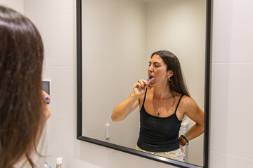 Woman performing daily oral hygiene routine, brushing teeth in her bathroom mirror