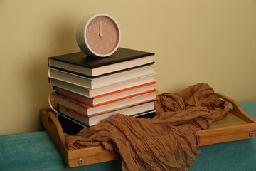 Collection of books and clock on a wooden tray on a couch during daylight