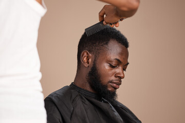 Side profile portrait of an adult African man with a trimmed beard and short natural hair wearing a barber cape during a professional grooming session in a studio setting. © The Yudel Media