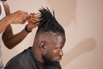Professional barber styling and refining locs on an adult African male client with a fresh fade haircut, highlighting precision grooming, textured natural hair, and modern men’s hairstyling in a clean