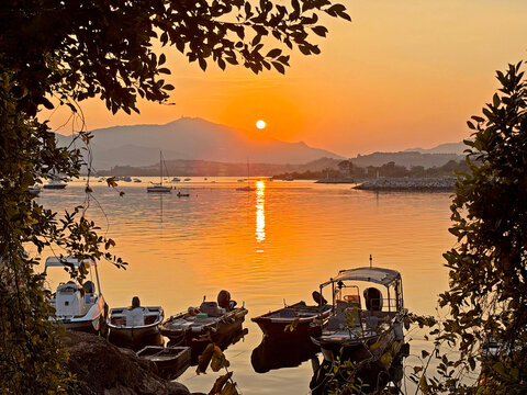 Serene sunset over a tranquil bay with moored boats and distant mountains - Powered by Adobe