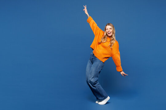Full body young happy woman she wearing yellow sweater casual clothes standing on toes dancing lean back have fun spreading hands isolated on plain blue background studio portrait. Lifestyle concept.