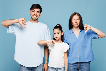 Young displeased sad parents mom dad with child kid daughter girl wearing casual clothes showing thumb down dislike gesture isolated on plain blue background. Family day parenthood childhood concept. © ViDi Studio