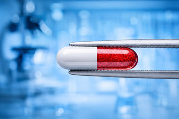 Red and white capsule held by laboratory tweezers