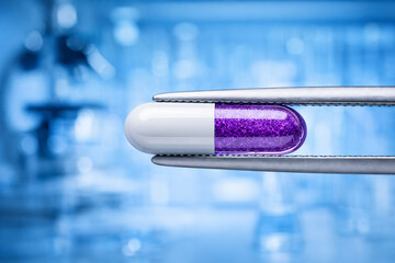 Purple and white capsule held by laboratory tweezers
