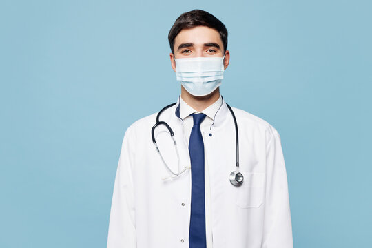Young confident male doctor man he wear white medical gown suit sterile mask work in hospital clinic office look camera isolated on plain blue background studio portrait. Healthcare medicine concept.